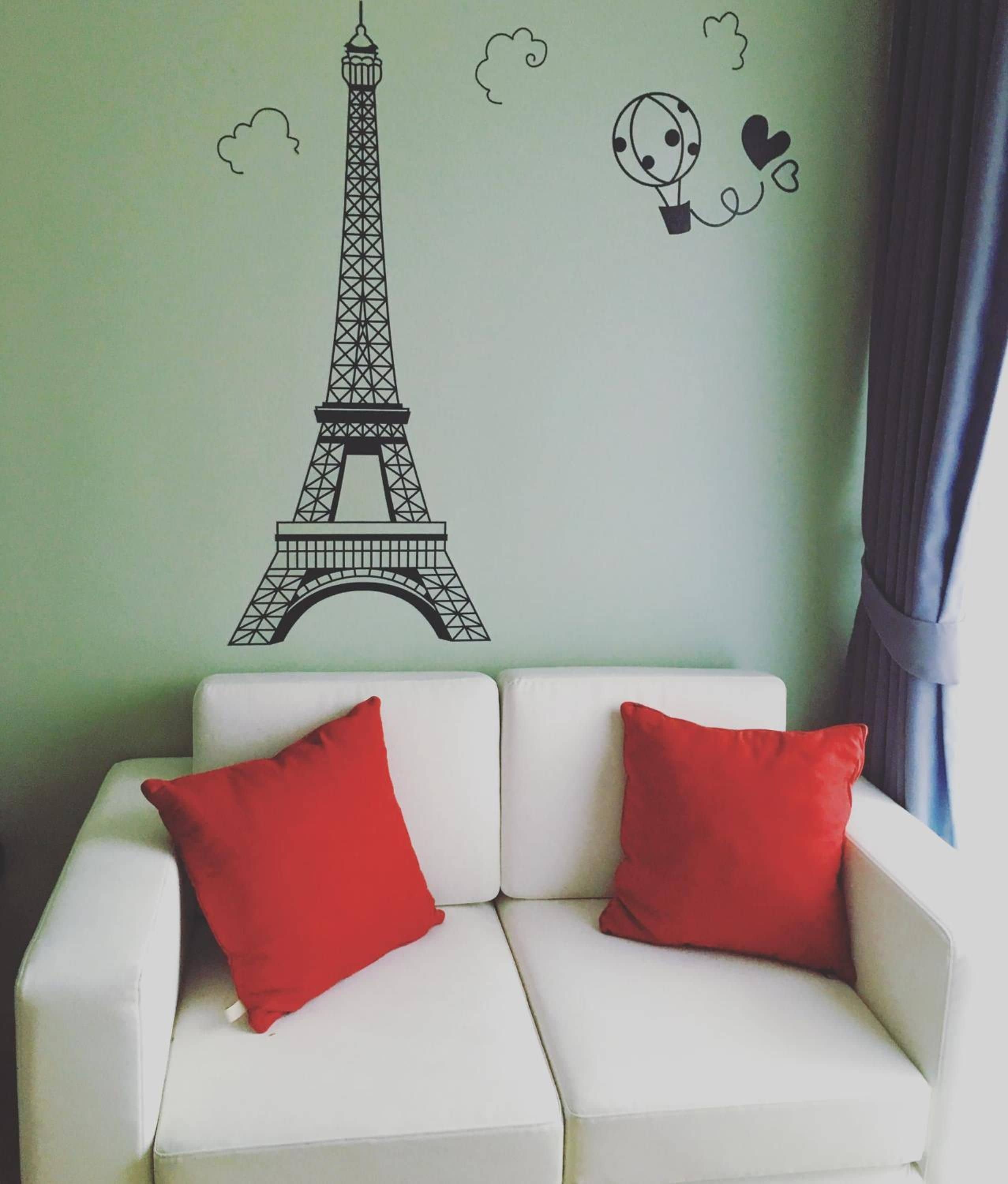 Ein weißes Sofa mit roten Kissen vor einer Wand mit einem Paris-Motiv.