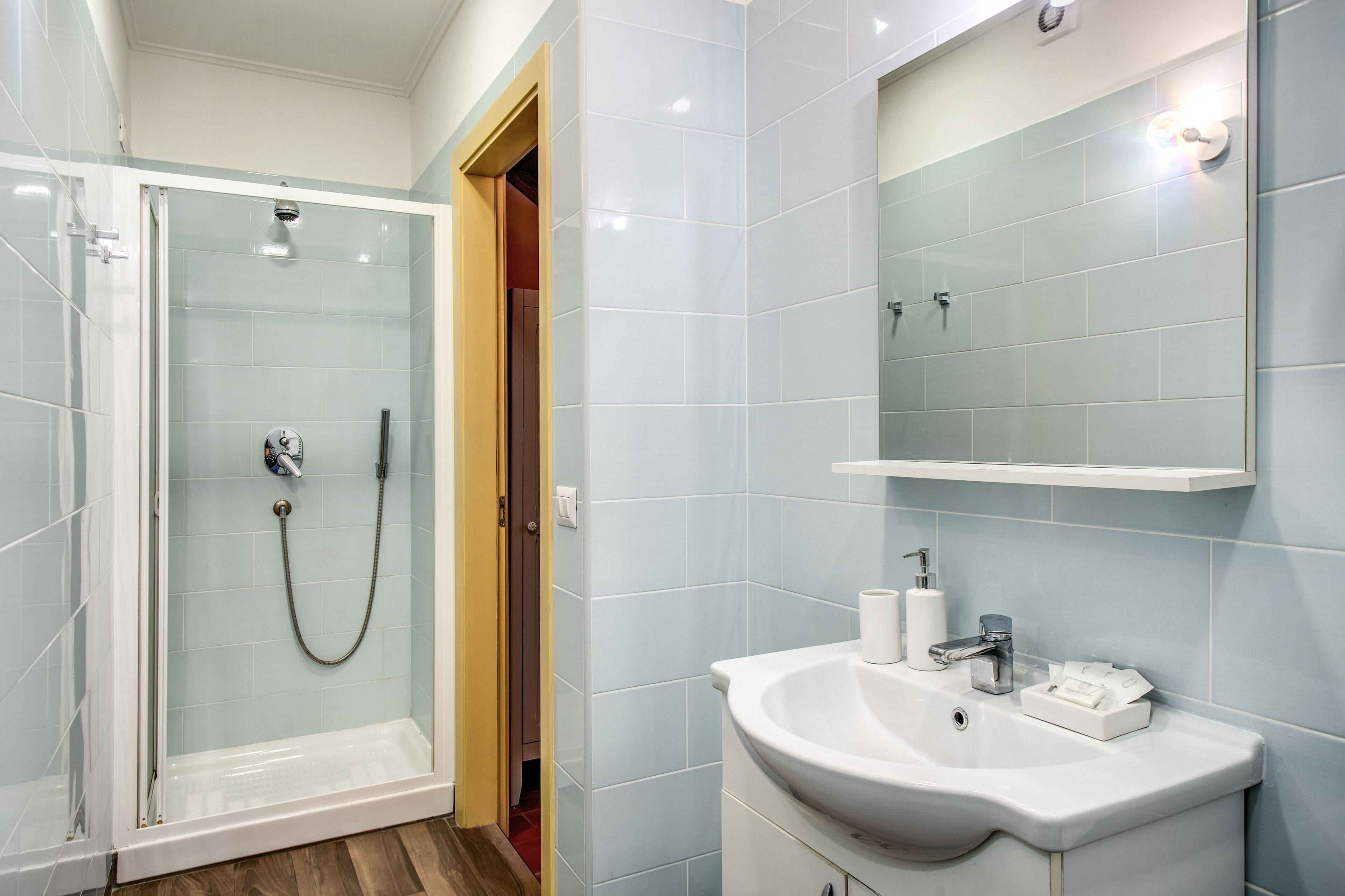 Un baño moderno con ducha envuelta en cristal, un lavabo blanco con espejo encima y azulejos azul claro en las paredes.