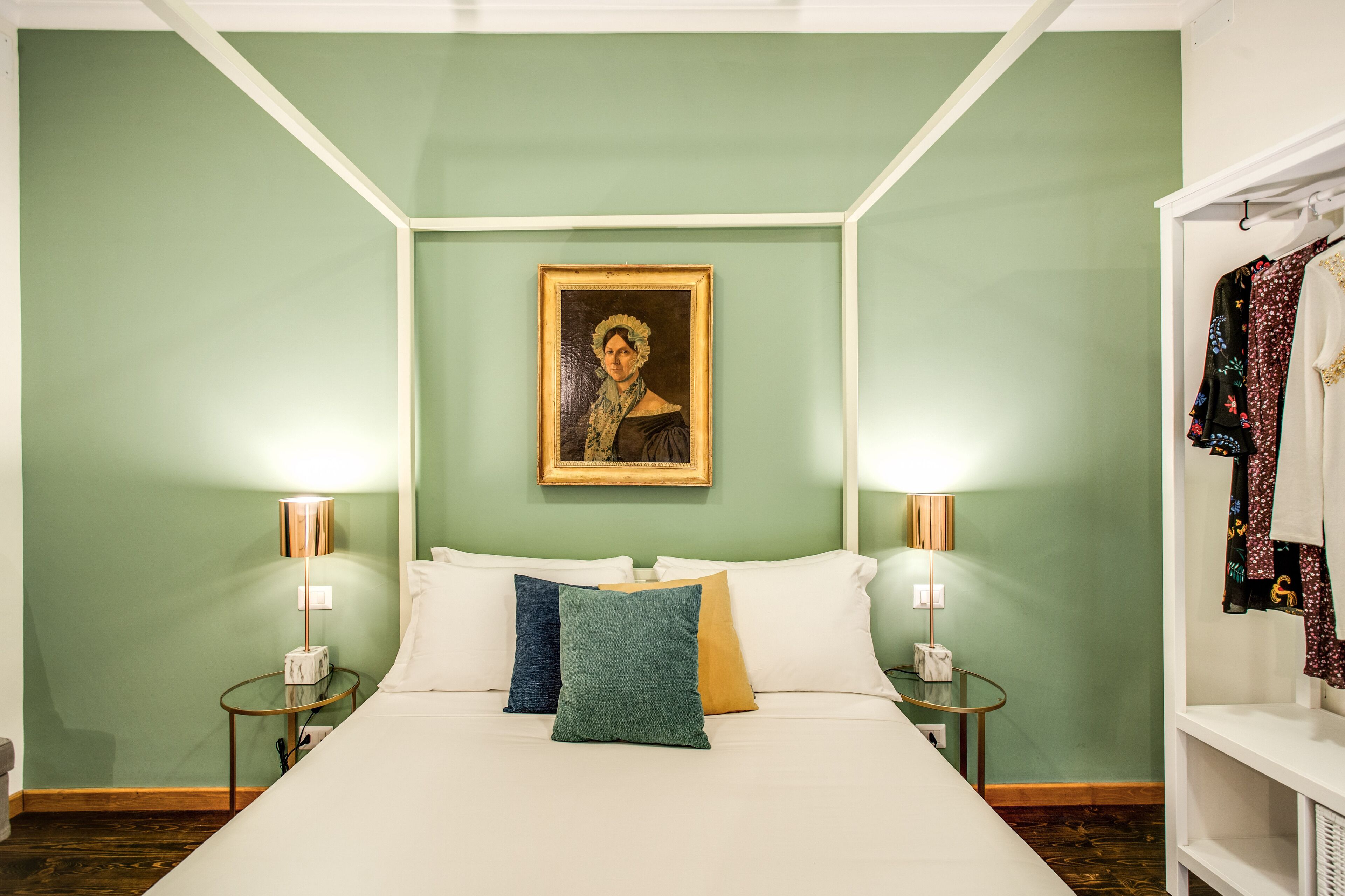 A neatly arranged bedroom with a bed, two bedside tables, a nightstand, a framed portrait on the wall, and a wardrobe.