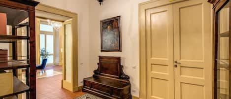 A hallway with a patterned rug, a wooden bench, a chandelier, and a door with a sign above it.