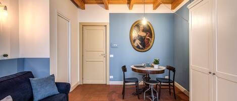 Un salon avec un canapé bleu foncé, une table de salle à manger ronde entourée de chaises, un plafond en bois et une armoire blanche.