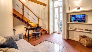A living room with a wooden staircase, a television on a shelf, and a cozy seating area.