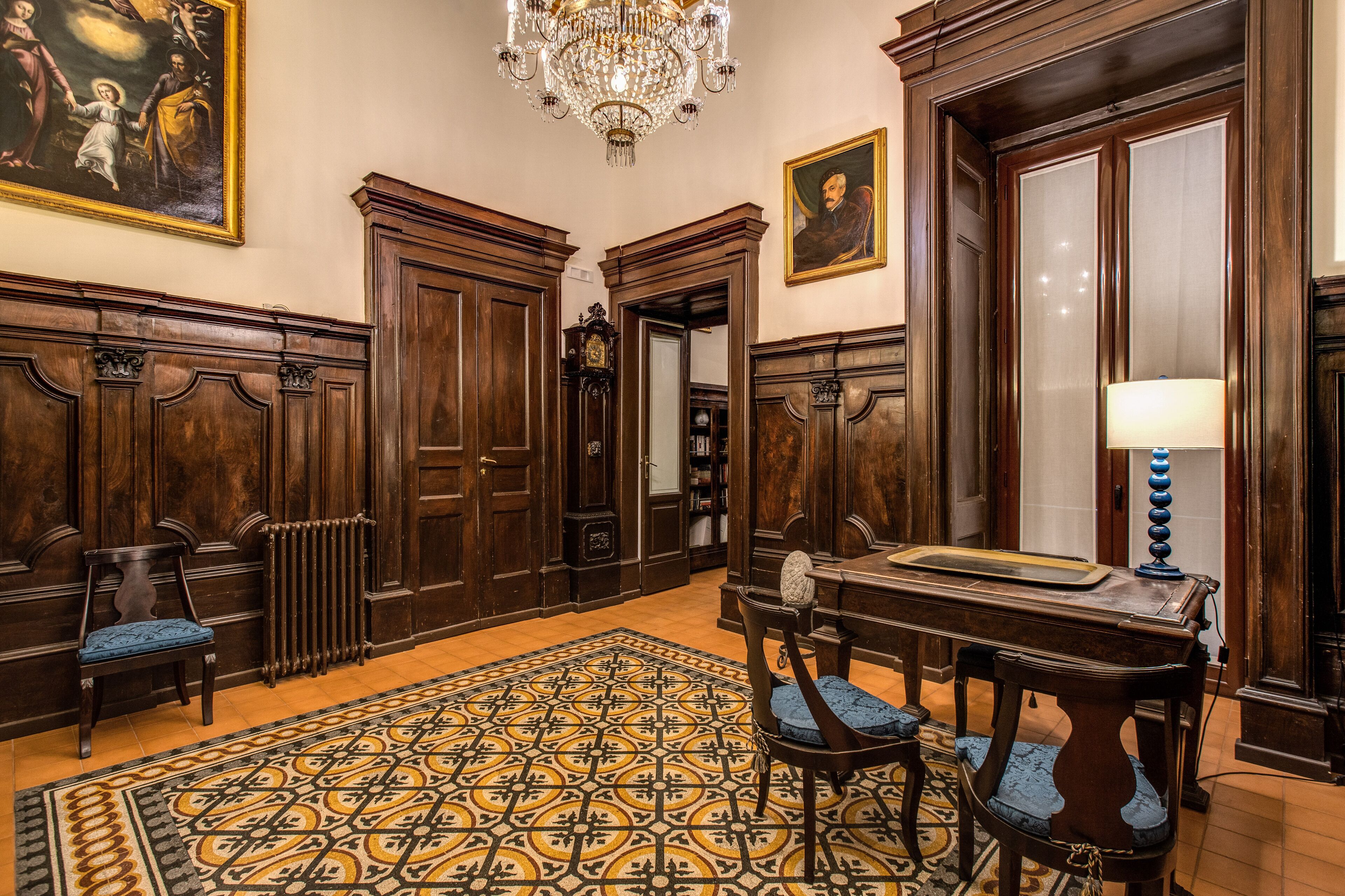 A room with wooden paneling, a chandelier, a patterned rug, and a table with chairs.