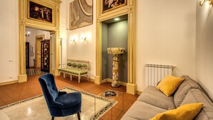 A spacious living room with a blue armchair, a grey sofa with yellow cushions, a patterned rug, and a marble floor lamp.