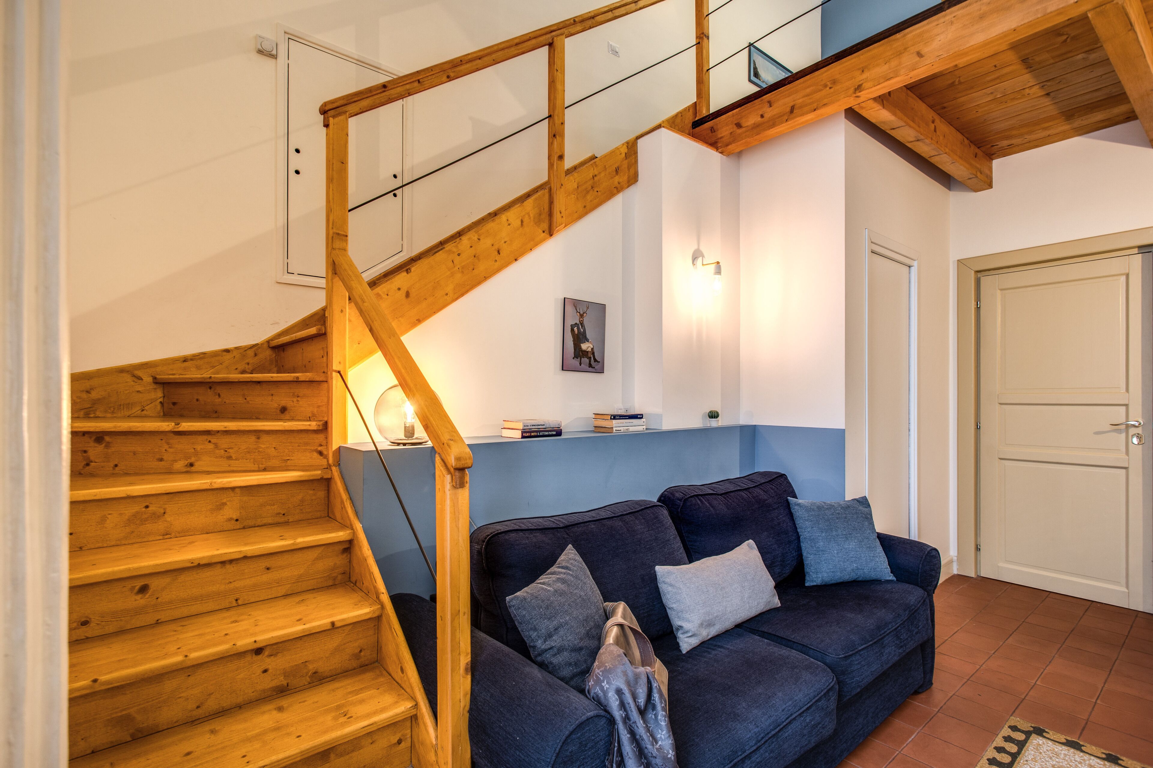 Una escalera de madera conduce a un rellano con un sofá azul y una puerta.