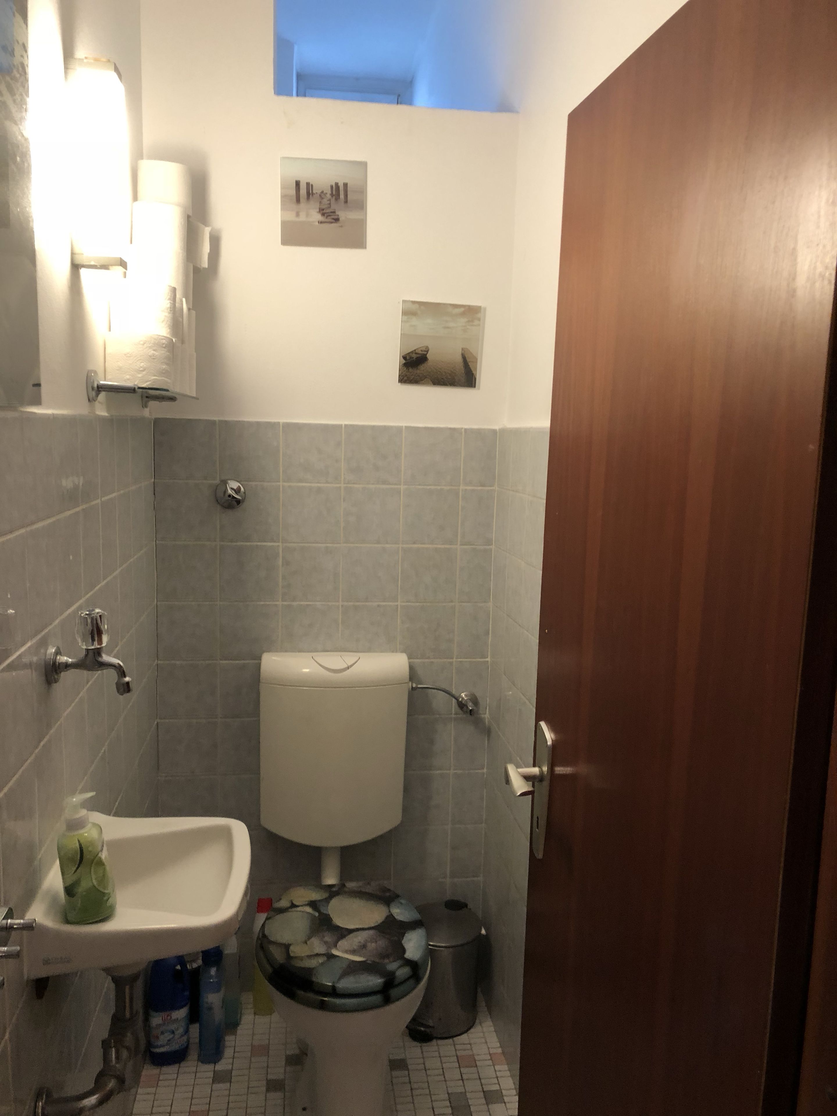 Ett badrum med toalett, handfat och dusch. Det finns tavlor på väggen och ett fönster ovanför toaletten.