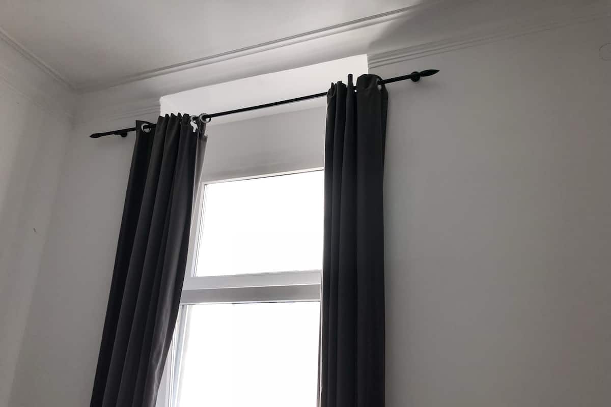 Una habitación con ventana, una barra para cortinas y una cortina.