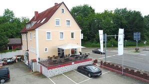Een gebouw met twee verdiepingen, een balkon en een overdekt terras, met een auto ervoor geparkeerd.