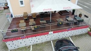 Een terras met tafels en stoelen, een Coca-Cola parasol en een bakstenen muur.