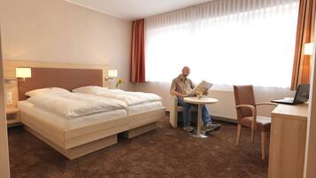Una habitación de hotel con una cama, un escritorio con una computadora portátil, una silla y una ventana con cortinas.