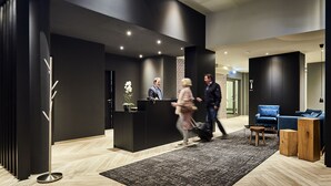 A modern reception area with a black reception desk, a wooden floor, and a blue seating area. - Hotel Hansa (Herford)