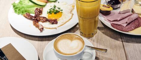Desayuno con platos de comida, un vaso de jugo de naranja y una taza de café con arte latte en forma de corazón.