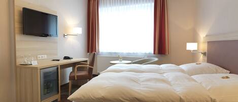 A hotel room with a bed, a desk with a television, a chair, and a window with curtains.