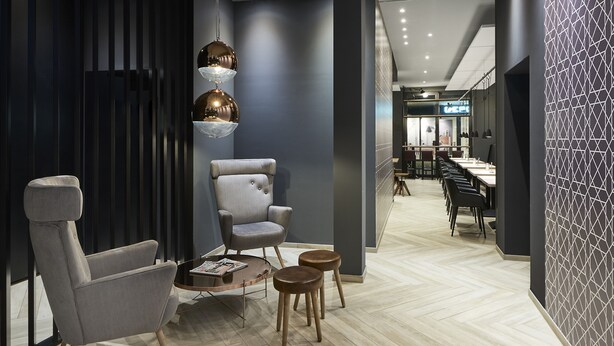 A modern lounge area with a grey armchair, a small table with a magazine, and a unique hanging light fixture. - Hotel Hansa (Herford)