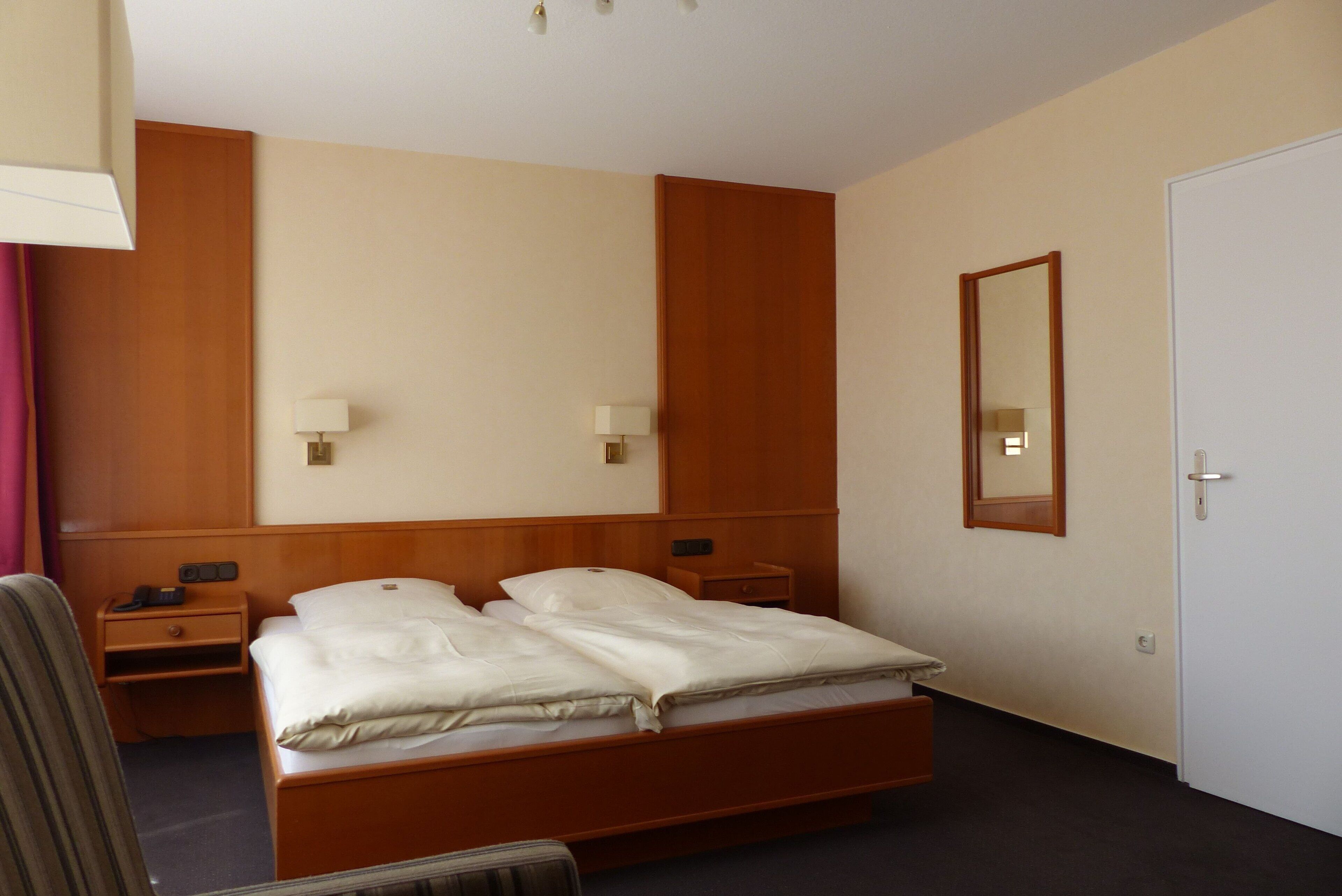 A hotel room with a double bed, two bedside tables, a nightstand, a lamp, a mirror, and a door.