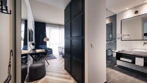 A modern hotel room with a large wardrobe, a separate bathroom, a dining area with a desk and chair, and a view of the city. - Hotel Hansa (Herford)
