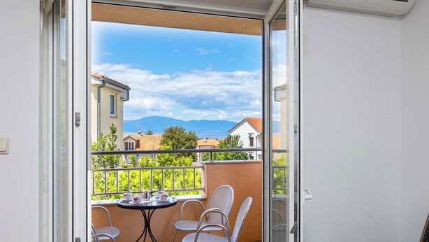Un balcon avec une table et des chaises, une vue sur la mer et les montagnes, et un bâtiment en arrière-plan.