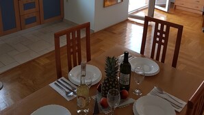 Un coin repas avec une table en bois dressée pour quatre personnes, une cuisine avec des meubles bleus et une porte-fenêtre coulissante donnant sur un balcon.