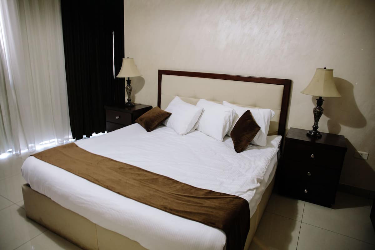 A hotel room with a large bed, two bedside tables, and a window with curtains.