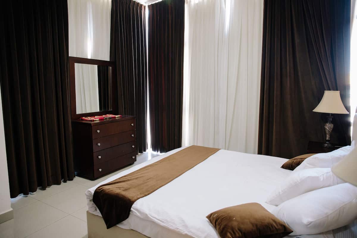 A bedroom with a bed, a dresser, a mirror, and curtains.