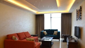 Ein modernes Wohnzimmer mit zwei Sofas, einem Couchtisch, einem Fernseher und einem großen Fenster mit Vorhängen.