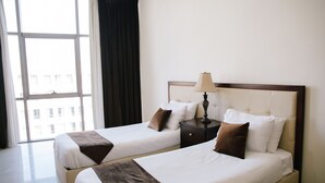Ein Hotelzimmer mit zwei Betten, einem Nachttisch mit Lampe und Blick auf Gebäude durch große Fenster.