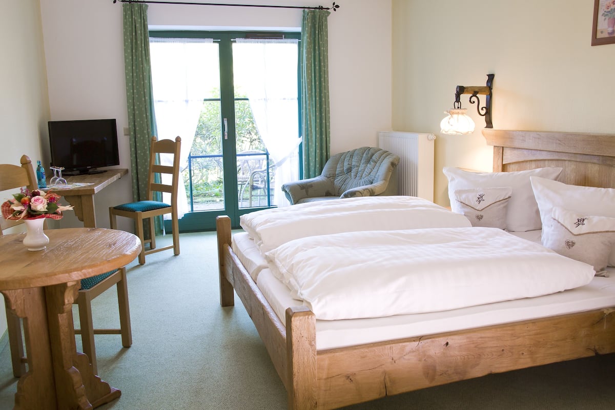 Een hotelkamer met een houten bed, een televisie, een tafel met een bloevas en een stoel.
