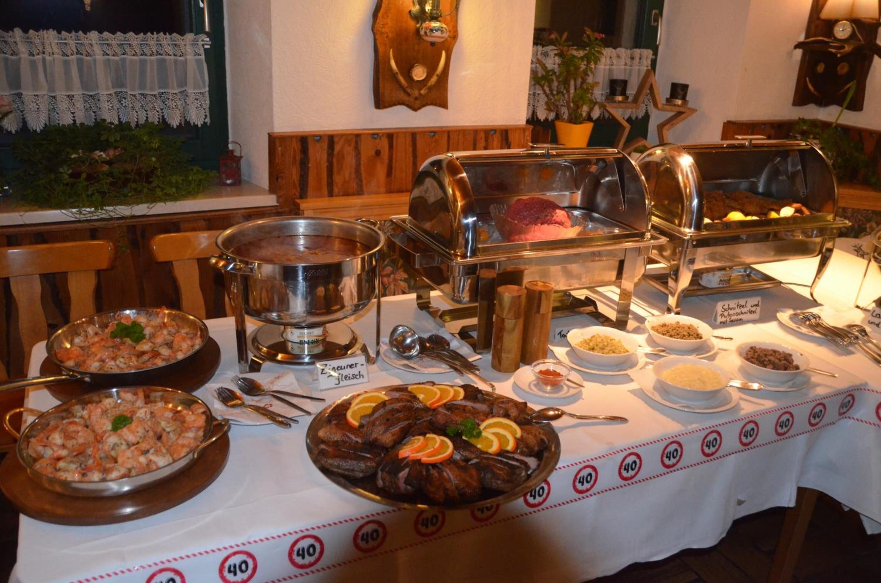 Une table de buffet proposant divers plats, notamment des fruits de mer et des viandes, ainsi qu’un panneau indiquant « Schwein-Fleisch » (viande de porc).
