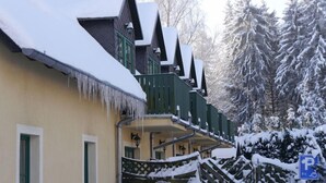 A snow-covered building with a steep roof and green railings. - Hotel Forsthaus Luchsenburg (Ohorn)