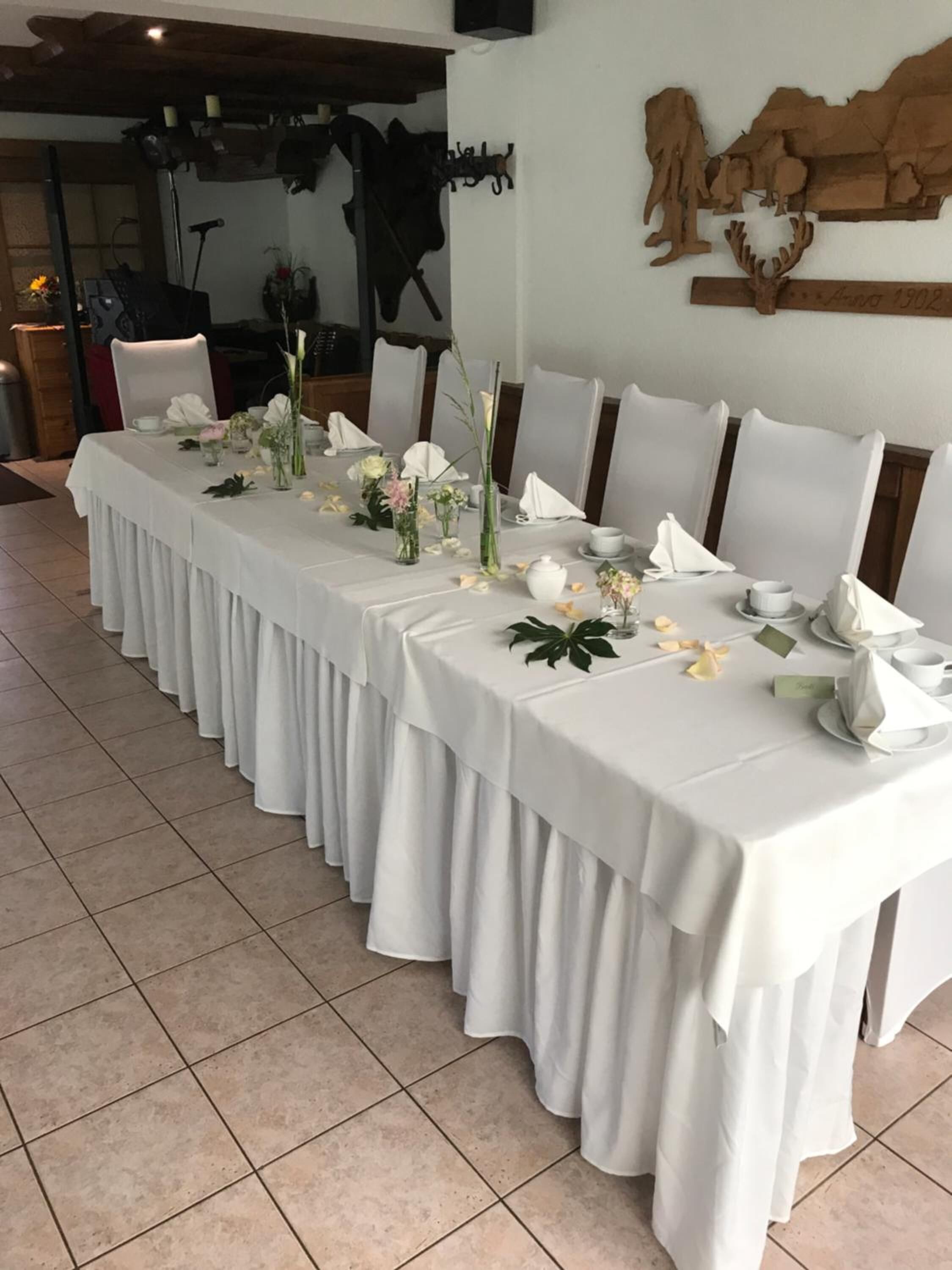 A long dining table set with white tablecloths, floral centerpieces, and neatly arranged place settings.