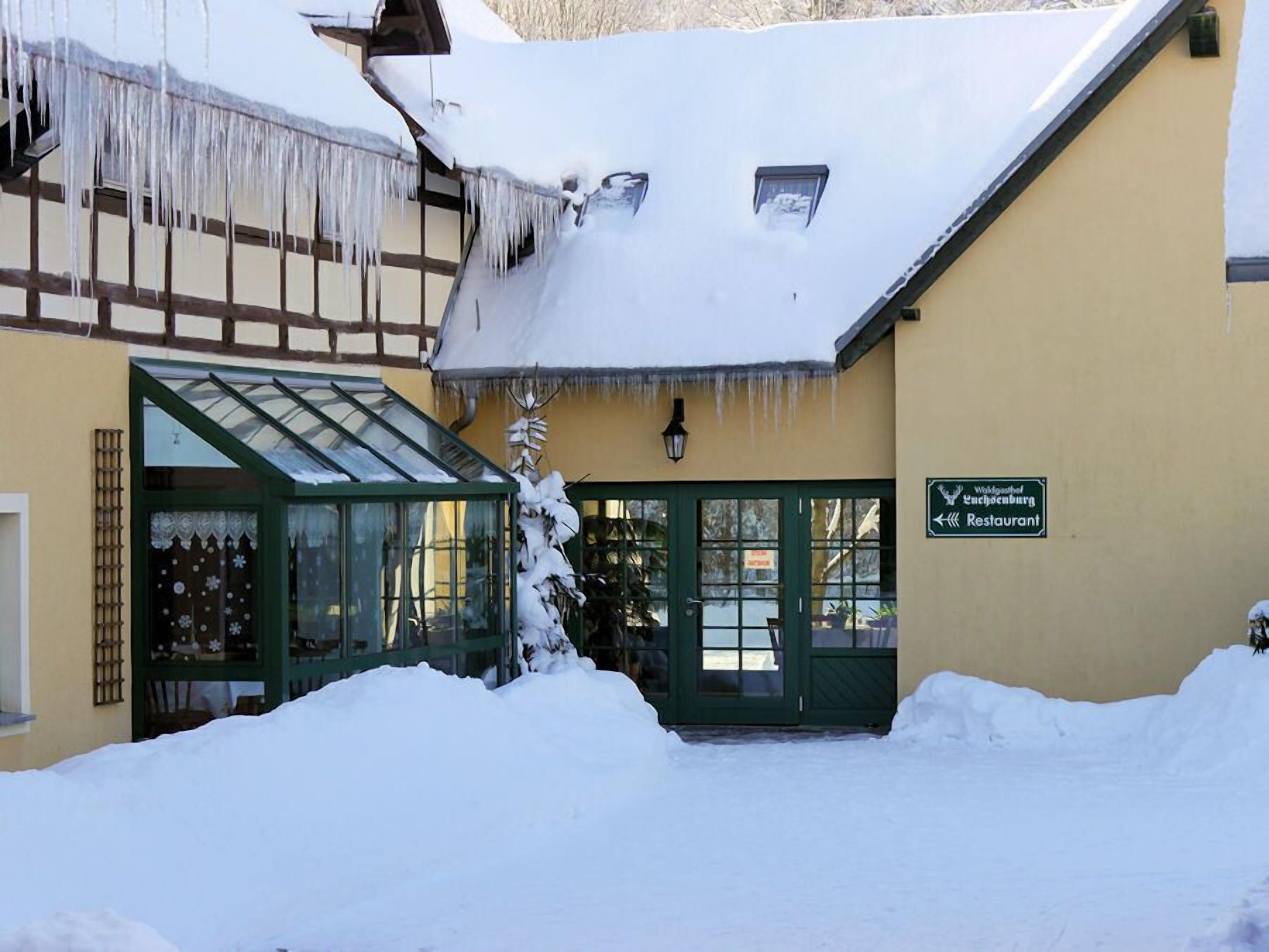 Un edificio con tetto innevato e stalattiti, una porta verde e un cartello che indica un ristorante.