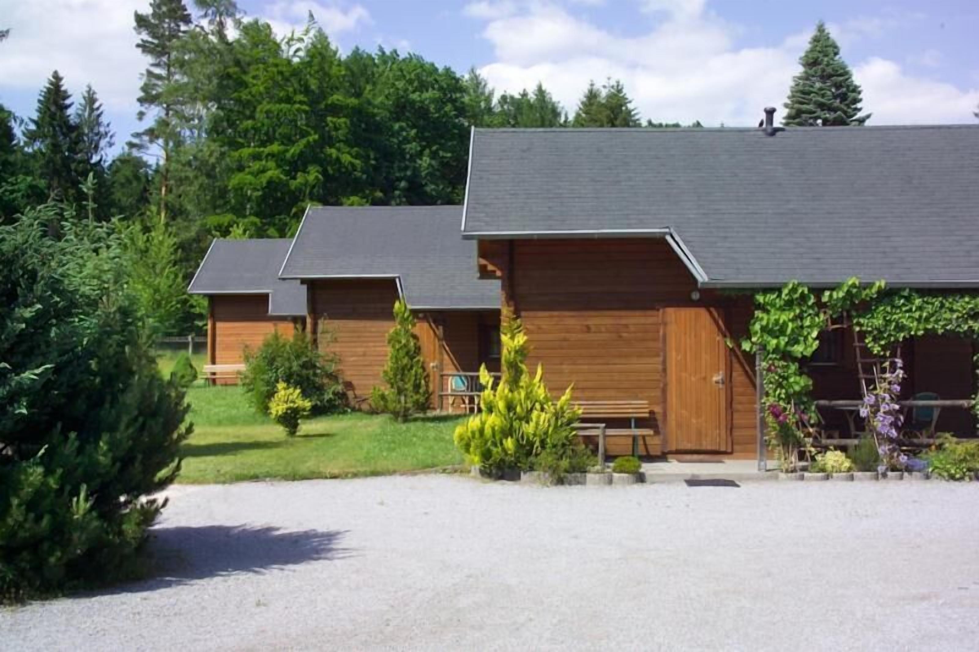 A row of wooden cabins with sloped roofs, surrounded by greenery and a gravel driveway.