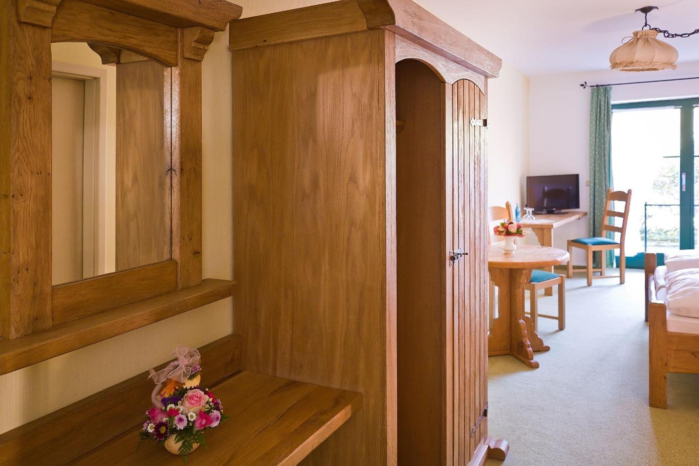 Una habitación con estructura de madera, con cama, escritorio y silla, televisor y ventana con cortinas.