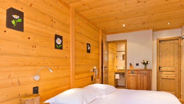 Una habitación de madera con una cama, un armario de madera, un espejo y una lámpara fijada a la pared.