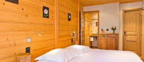 A wooden room with a bed, a wooden cabinet, a mirror, and a wall-mounted light fixture.
