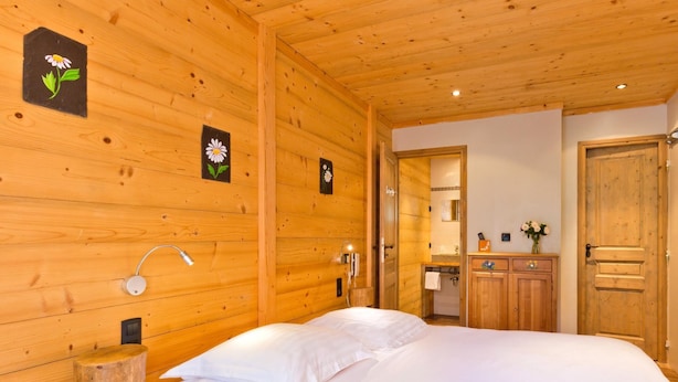 A wooden room with a bed, a wooden cabinet, a mirror, and a wall-mounted light fixture. - Logis Hotel L'accueil Savoyard (Mieussy)