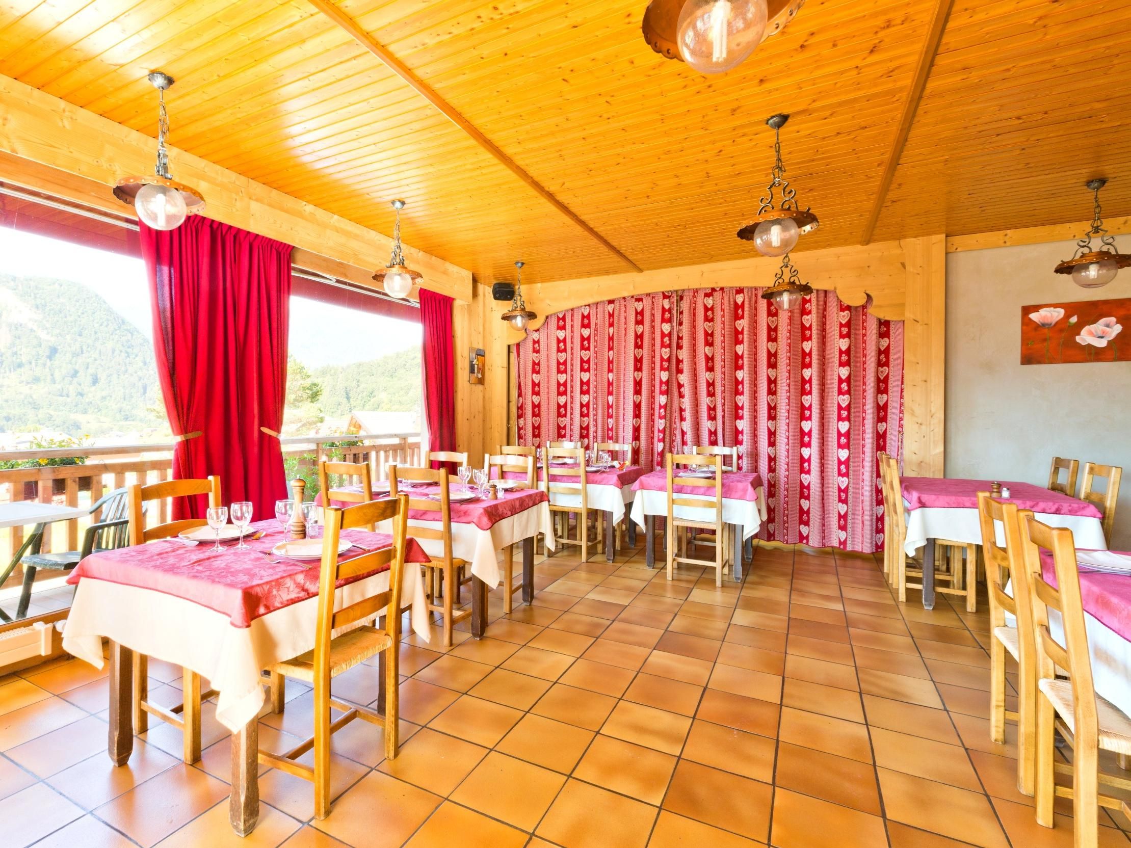 A restaurant with wooden tables and chairs, red curtains, and a view of the outdoors.