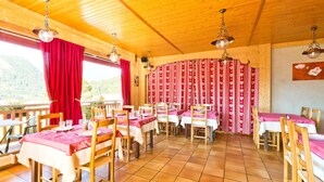 Un restaurante con mesas y sillas de madera, cortinas rojas y vistas al exterior.
