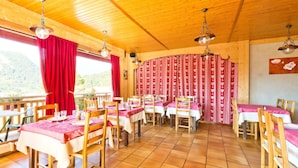 A restaurant with wooden tables and chairs, red curtains, and a view of the outdoors. - Logis Hotel L'accueil Savoyard (Mieussy)