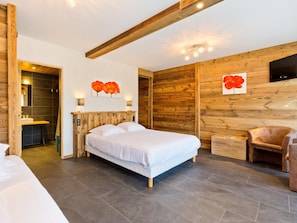 A bedroom with a wooden ceiling, a bed, a chair, and a TV mounted on the wall. - Logis Hotel L'accueil Savoyard (Mieussy)