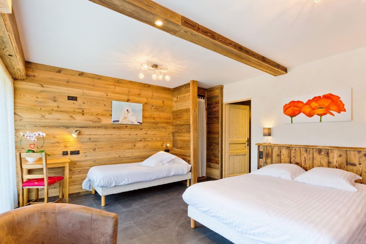 Una habitación con dos camas, paredes y techo de madera, una mesita con una silla y un cuadro de flores.