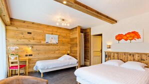 Ein Zimmer mit zwei Betten, Holzwänden, Holzboden und einem kleinen Tisch mit einem Stuhl, sowie einem Blumenbild.