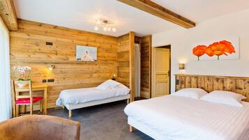 Una habitación con dos camas, paredes y techo de madera, una mesita con una silla y un cuadro de flores.