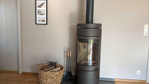 Ein moderner Kaminofen mit Glastür, ein Holzkorb und ein gerahmtes Bild an der Wand.