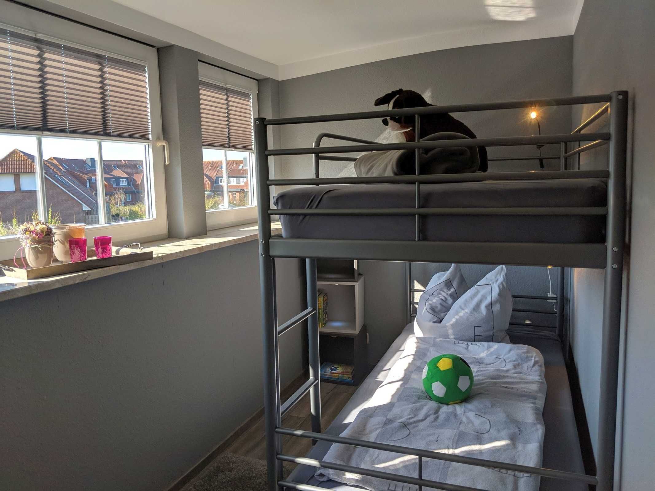A bunk bed room with a dog on the top bunk, a window with blinds, and a soccer ball on the bottom bunk.