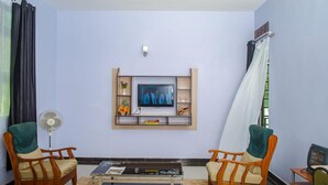 A living room with a TV, two chairs, a coffee table, and a fan. - The Starbucks Hotel (Eldoret)
