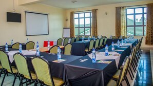 A conference room with long tables, chairs, water bottles, and a projector screen. - The Starbucks Hotel (Eldoret)