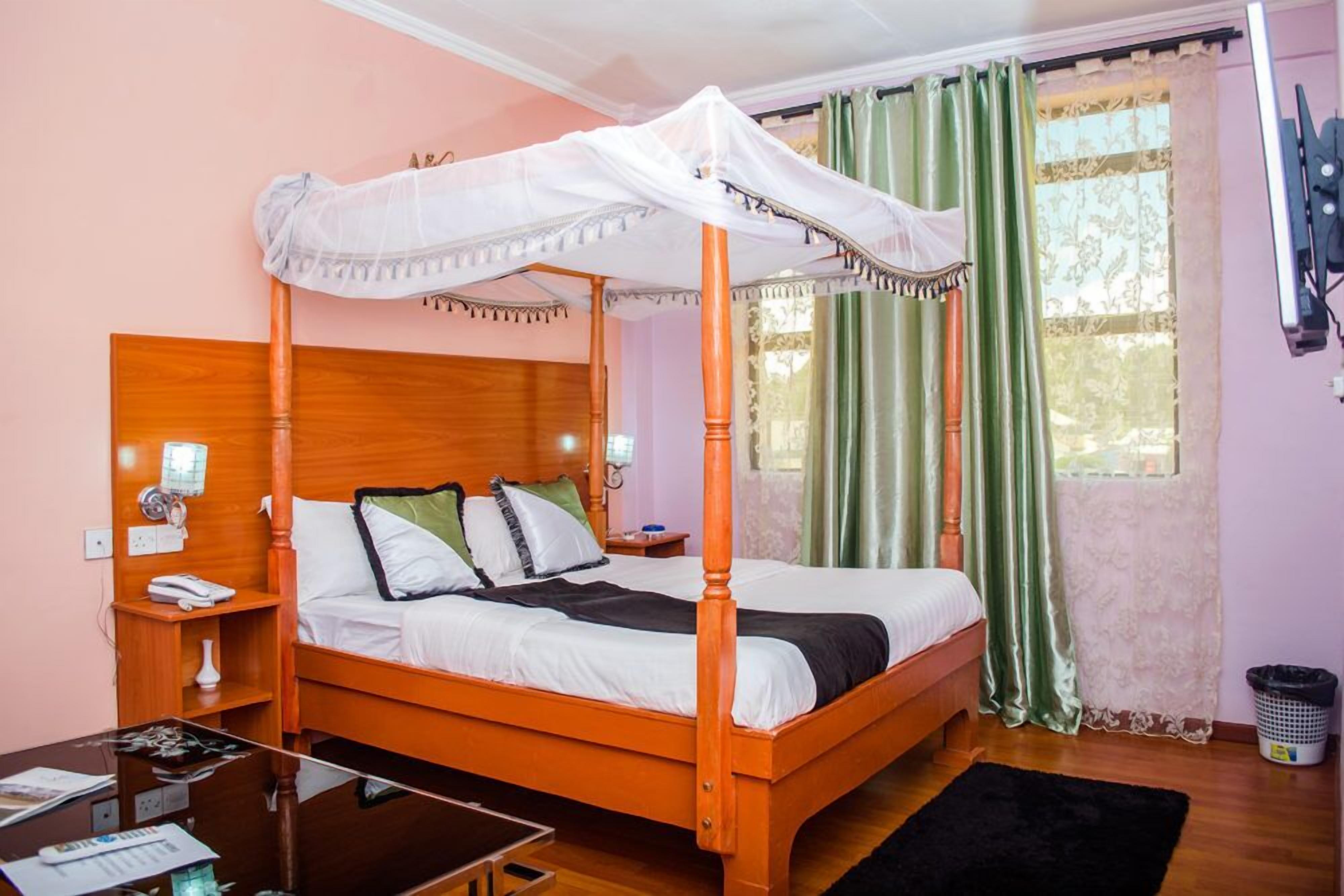 A four-poster bed with a canopy, a bedside table with a lamp, and a view of a window with curtains.