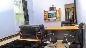 A modern office space with a black leather sofa, two black office chairs, a wooden desk, and a television on a shelf. - The Starbucks Hotel (Eldoret)