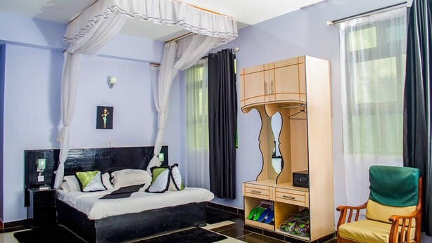 A bedroom with a four-poster bed, a wooden wardrobe, a chair, and a shoe rack. - The Starbucks Hotel (Eldoret)